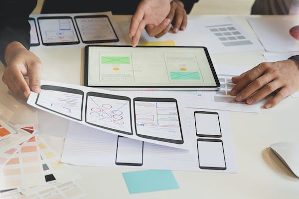 Wireframing and designing process for Civic Opportunity Project, there are hands pointing to a tablet and papers of the low fidelity prototyping.